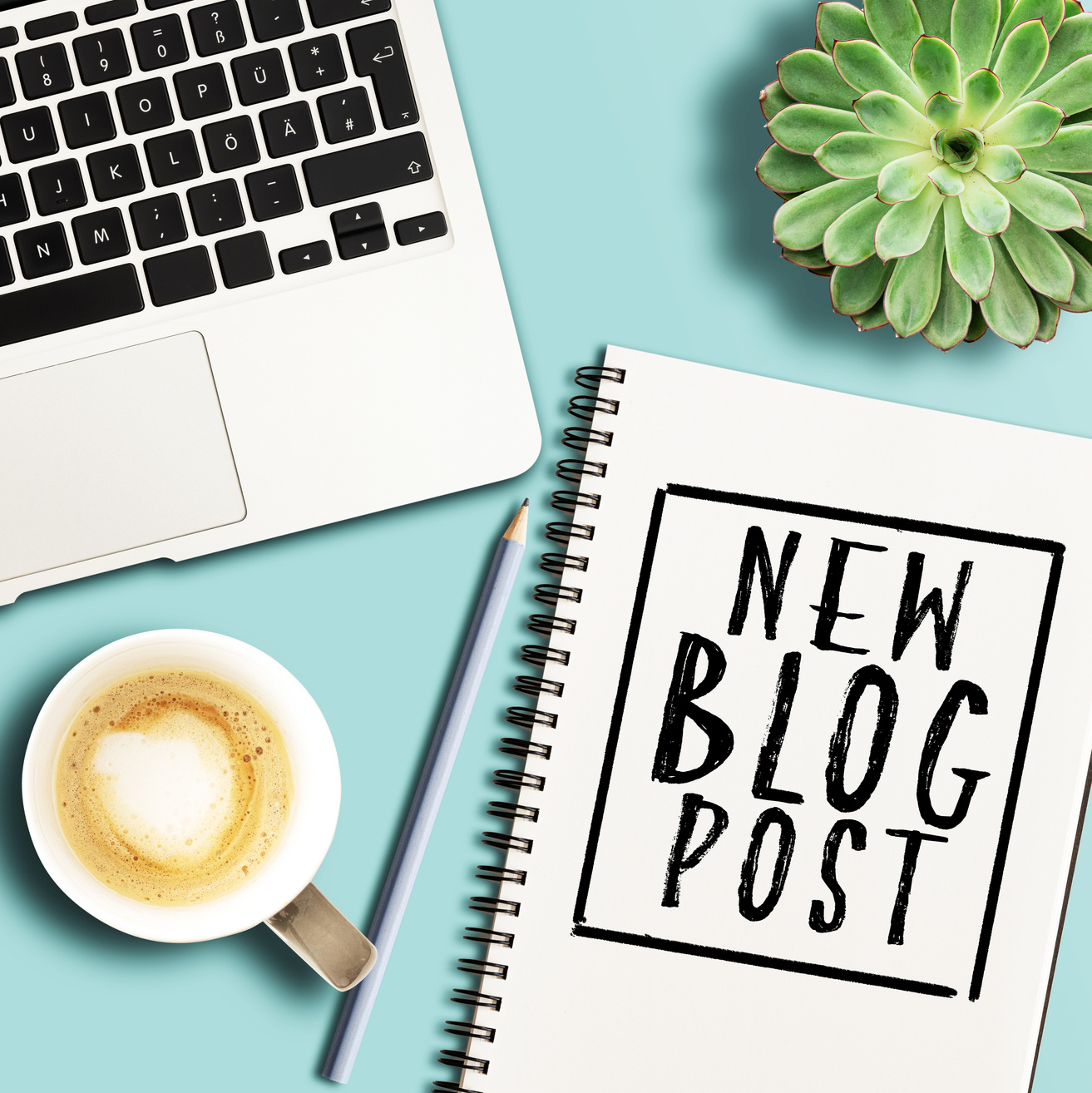 words NEW BLOG POST written on spiral notepad on desk with laptop and potted plant